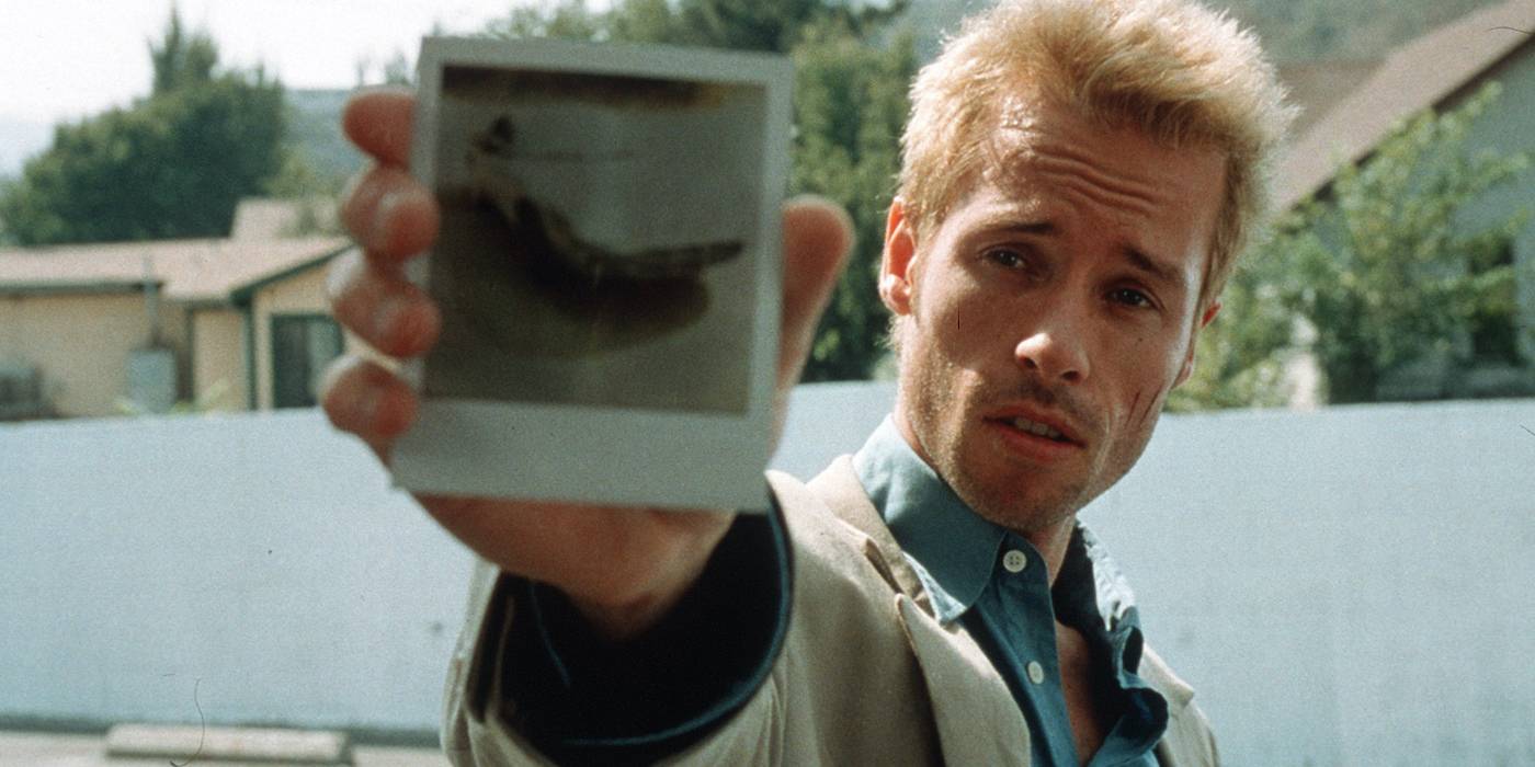 Thrillers psicológicos: 10 filmes com roteiro impecável Guy Pearce como Leonard Shelby, estendendo uma polaroid em Memento.