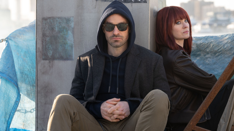 Charlie Cox as Matt Murdock wearing sunglasses and sitting next to Deborah Ann Woll as Karen Page in a wig in Daredevil: Born Again