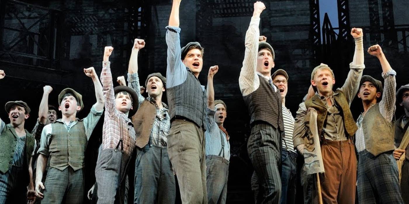 The Newsies raise their fists to the sky at the end of Seize the Day in Newsies: The Broadway Musical