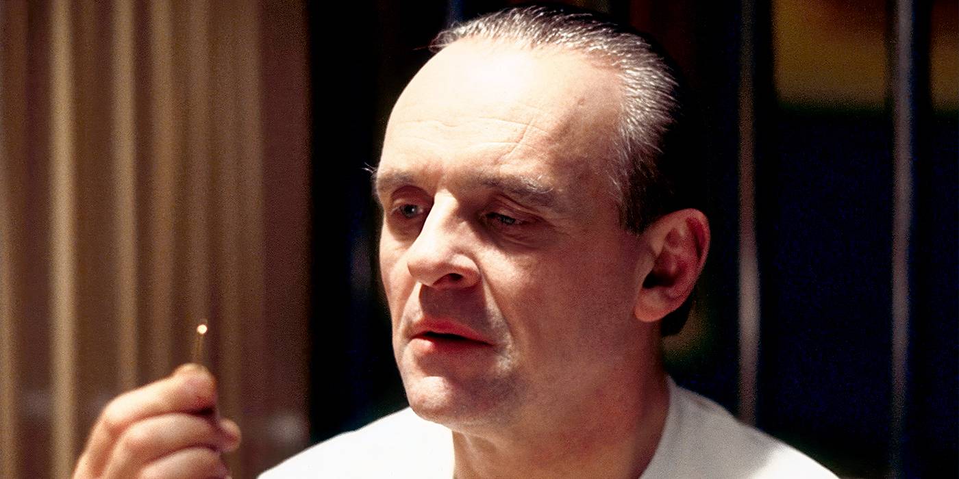 Thrillers psicológicos: 10 filmes com roteiro impecável Anthony Hopkins olhando intensamente para um pequeno objeto de metal em The Silence of the Lambs.