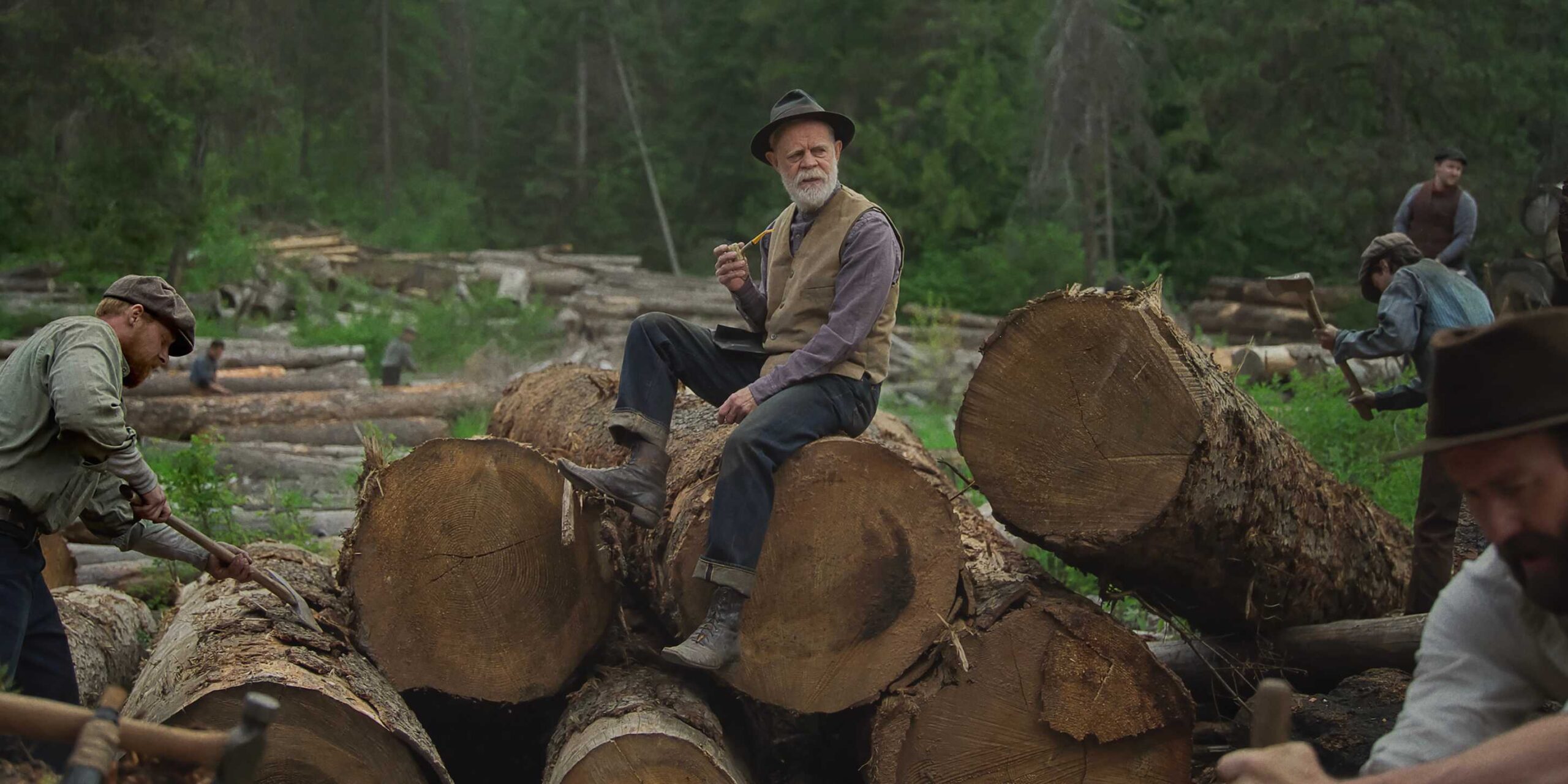 Arn Peeples (William H. Macy) sitting on tree logs in Train Dreams