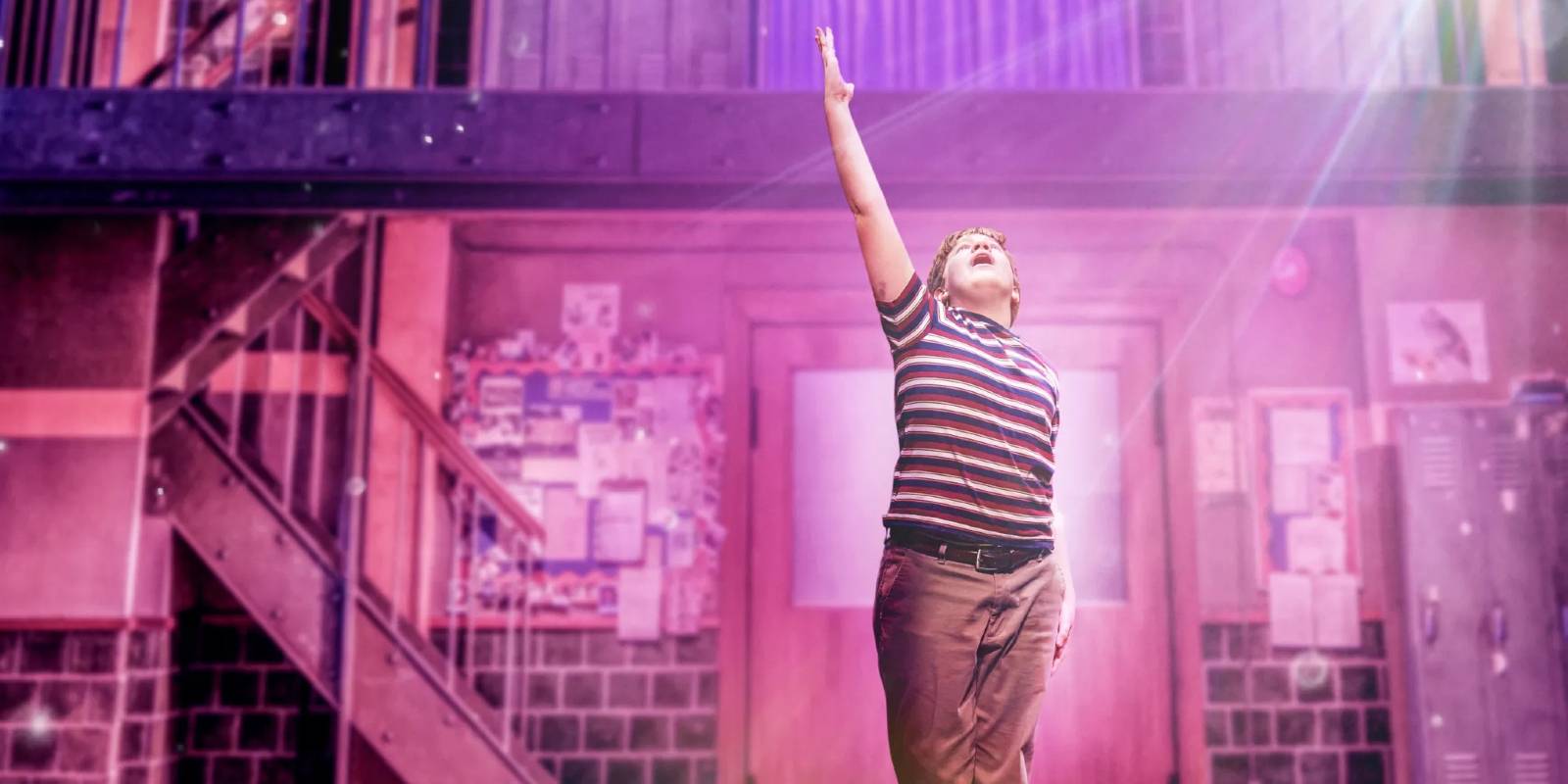 Trevor reaches up to the sky in pink lighting in Trevor The Musical proshot